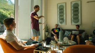 four men holding laptops and talking in a living room